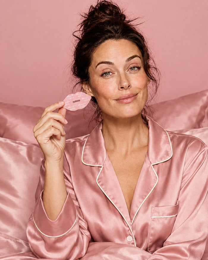 A woman pressing a pink lip-shaped Beauty Sleep strip onto her lips